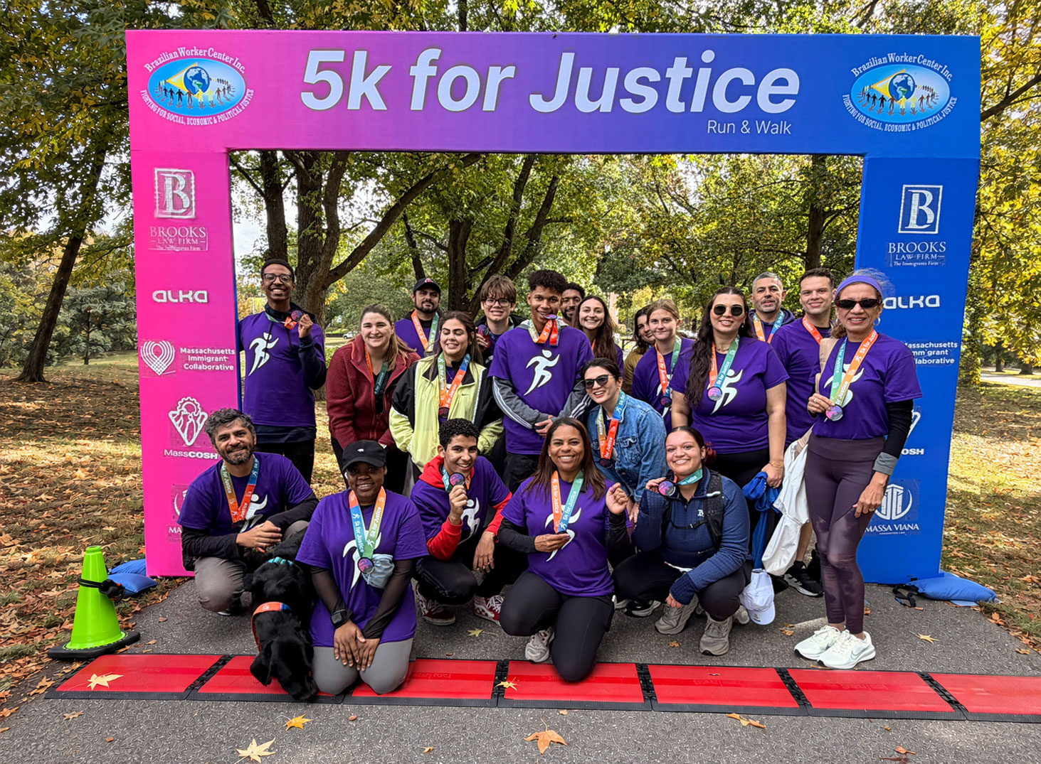 Participants of the 5K for Justice Run & Walk posing with medals and a dog under the finish arch